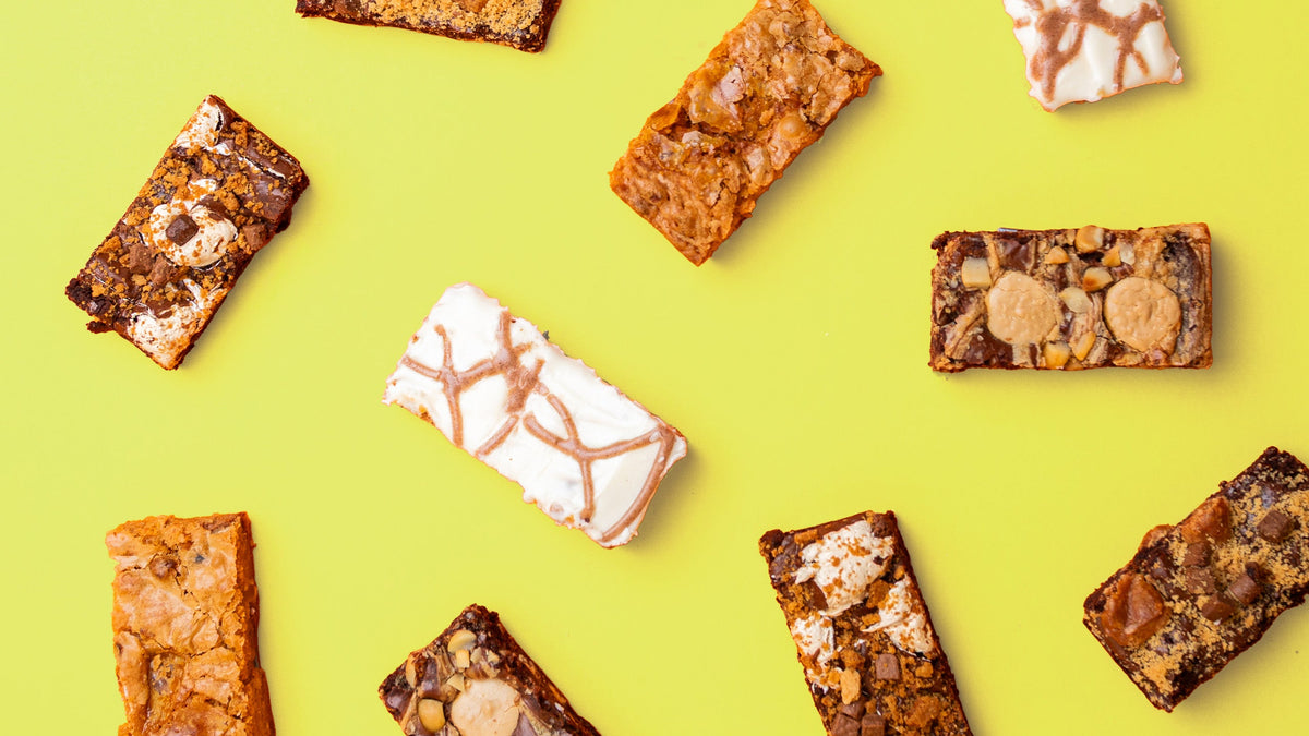 An overhead flat-lay of assorted brownie bars arranged on a bright yellow background.