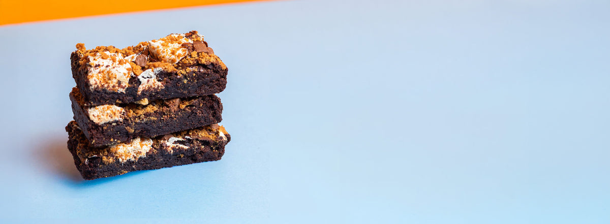 Three stacked brownies, positioned on the left side of a light blue background with a small orange accent at the top.