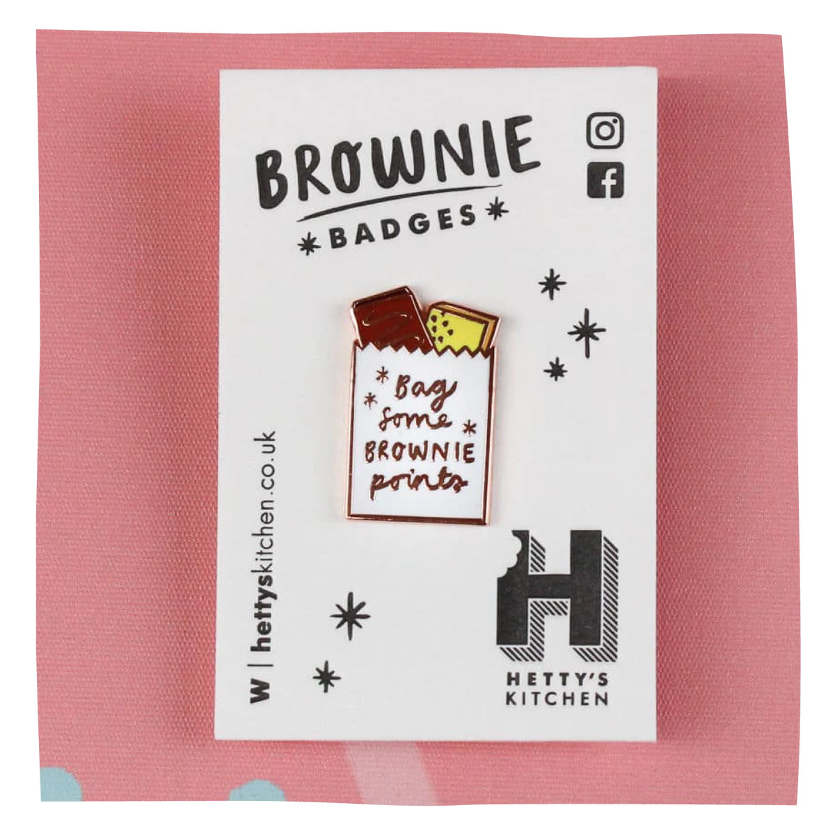 A brownie badge pin displayed on its white branded backing card, set against a pink textured background. 