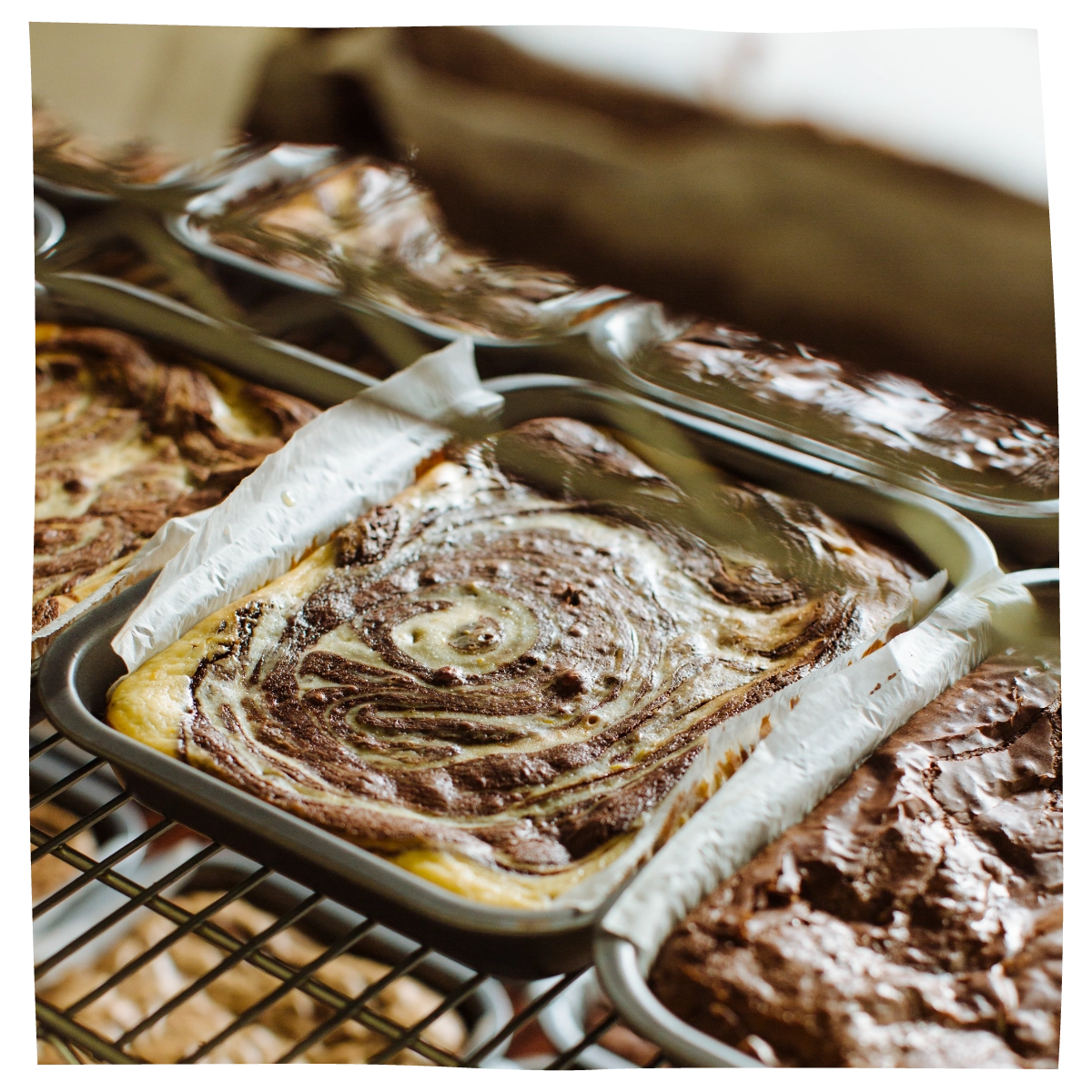 Baked brownie bars in metal pans lined with parchment paper, arranged on a cooling rack. 