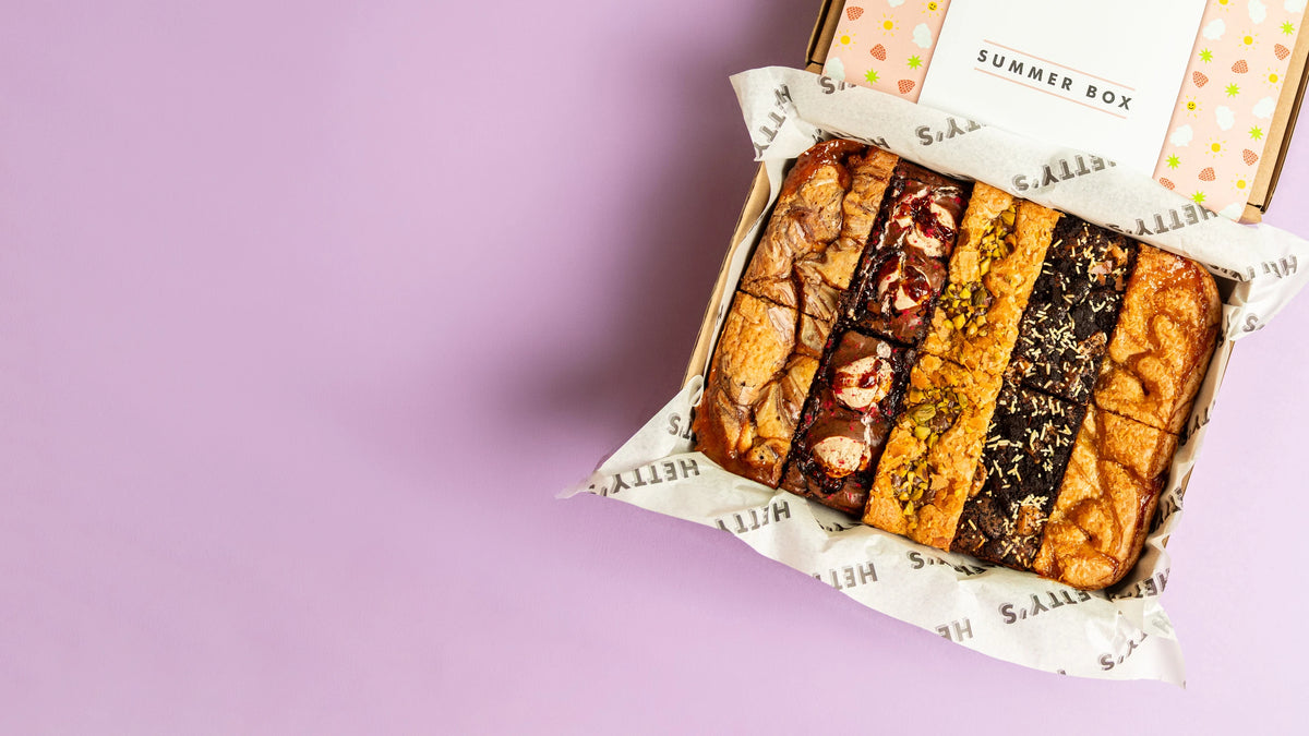 An open cardboard box filled with assorted brownies, lined with branded paper. 