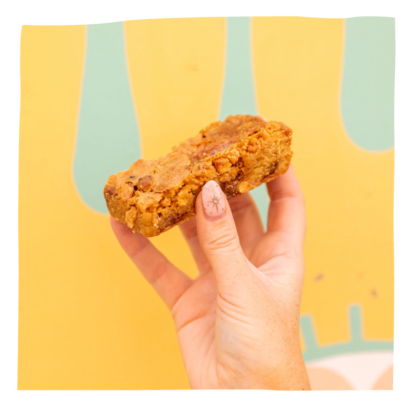 A hand holding a square, golden-brown baked brownie