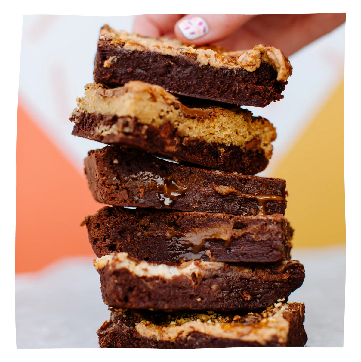 A close-up of a hand stacking five thick, layered chocolate brownies