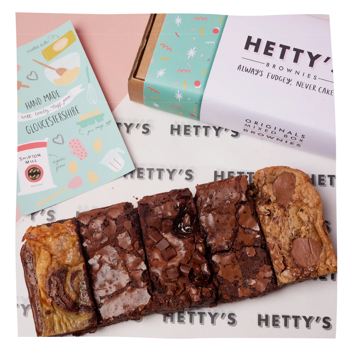 Six chocolate brownies arranged on a branded white tray with repeated HETTY'S text, alongside a pastel card and a decorated brownie box. 