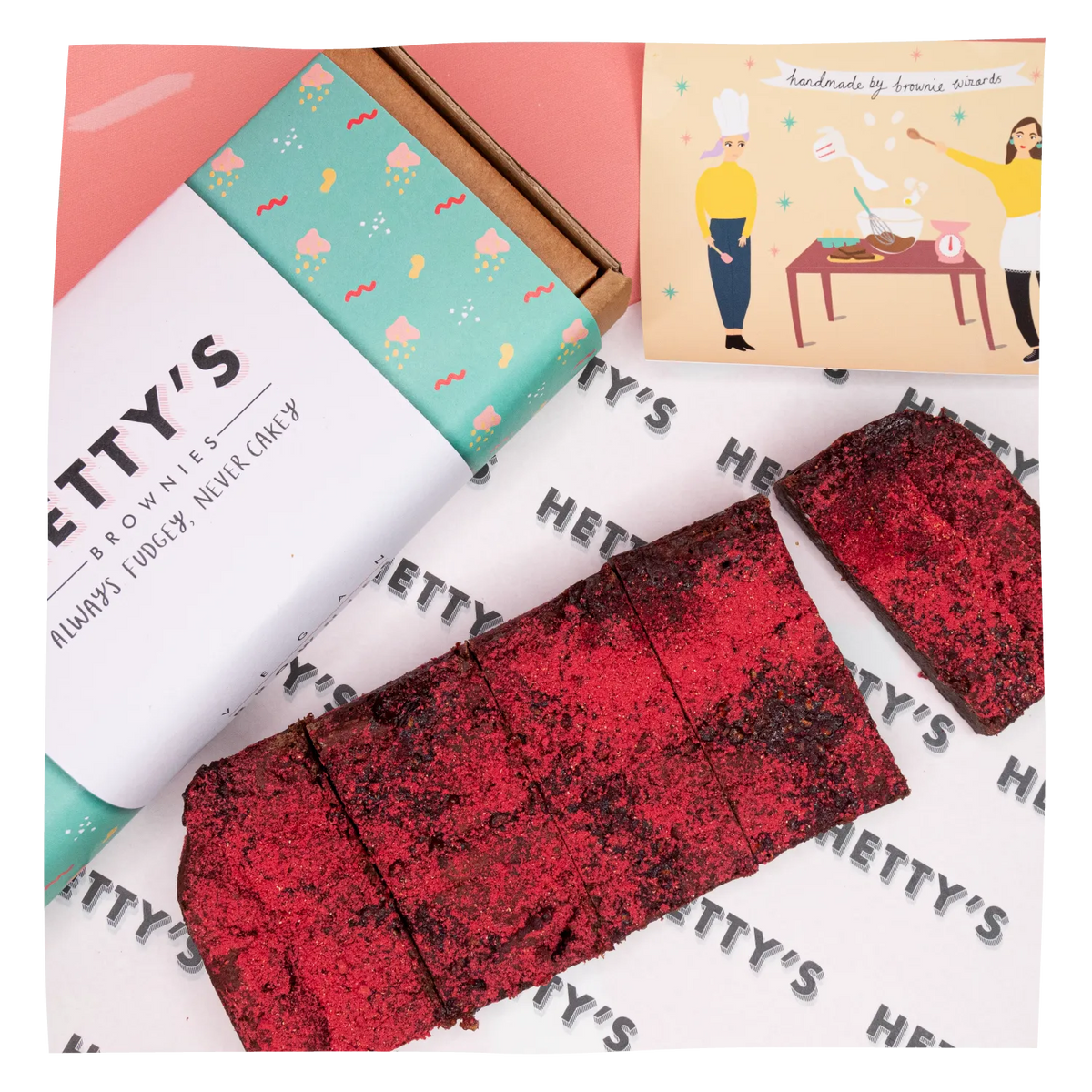 A styled product shot of Hetty's Brownies featuring a white and mint green branded box, a printed brand card, and several cut brownie bars dusted with red sugar on a branded paper surface.