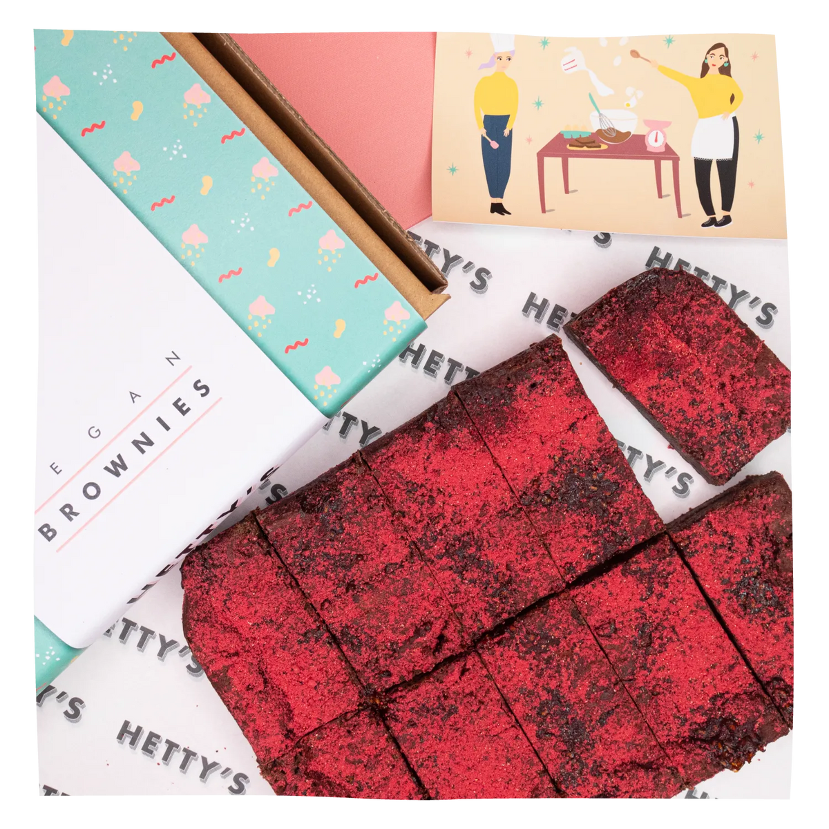 A styled product shot of Hetty's Brownies featuring a white and mint green branded box, a printed brand card, and several cut brownie bars dusted with red sugar on a branded paper surface.