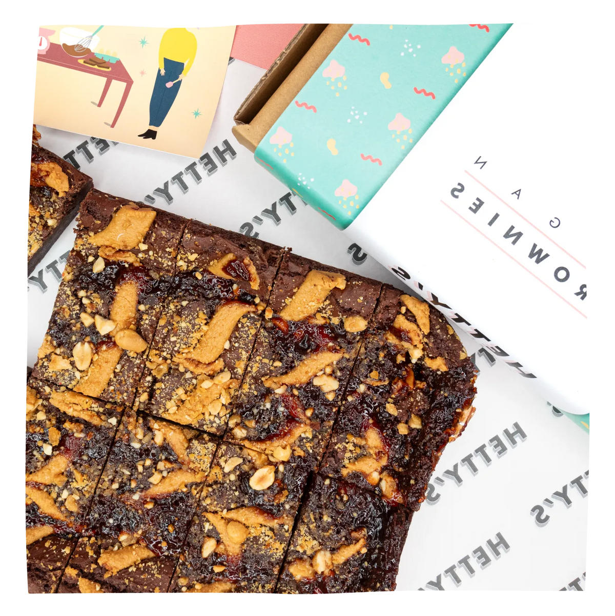 A top-down styled product shot of chocolate brownies , arranged on branded paper next to a mint gift box and a small card.