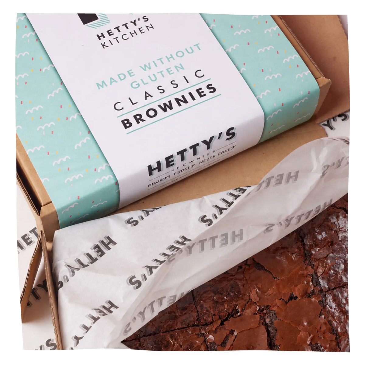 A boxed product labeled 'Hetty's Kitchen Made without Gluten Classic Brownies' sits open with tissue paper and a brownie visible, photographed on a white background.