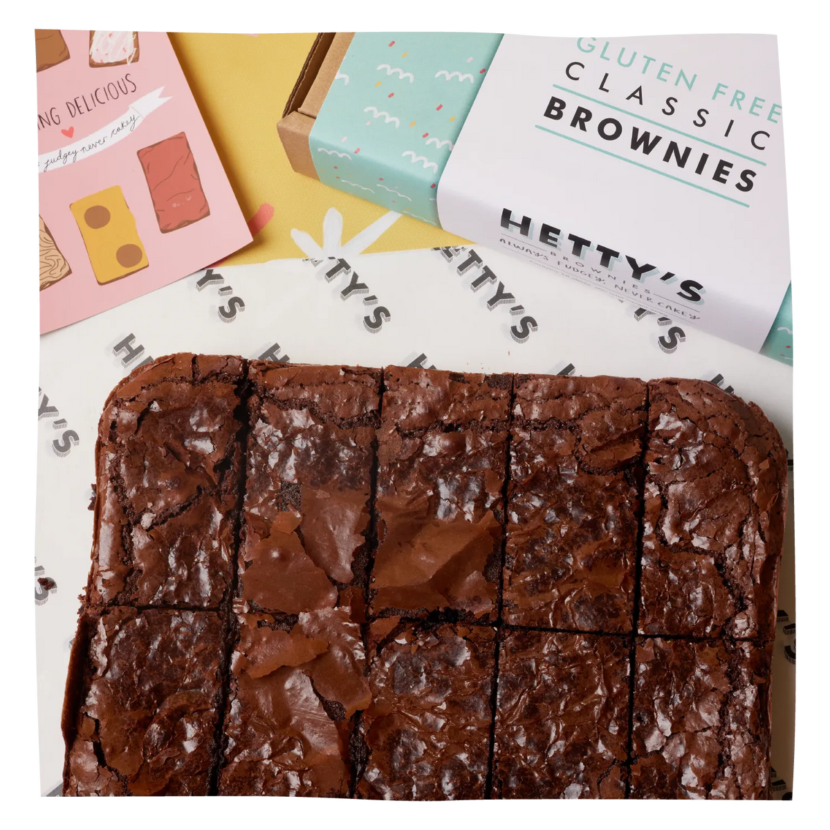 A square arrangement of freshly baked chocolate brownies cut into slices, with a box labelled 'Hetty's Gluten Free Classic Brownies.'