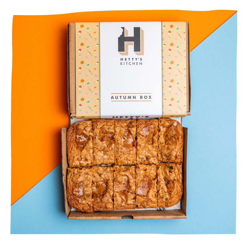 An open cardboard box of baked goods from Hetty's Kitchen, labeled 'Autumn Box,' showing several golden-brown square brownies.