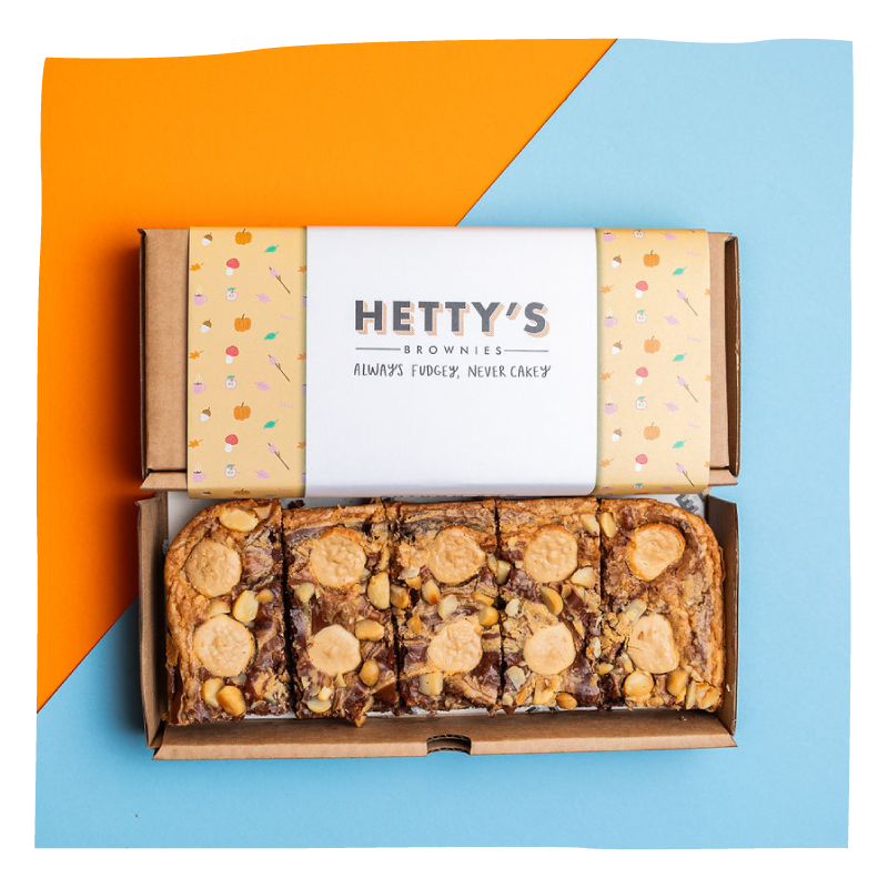 An open cardboard box of Hetty's Brownies, set against a diagonally split orange and light blue background.