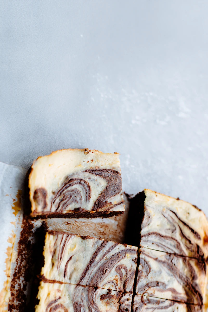 A close-up overhead shot of a sliced brownie, cut into pieces on a light gray surface.