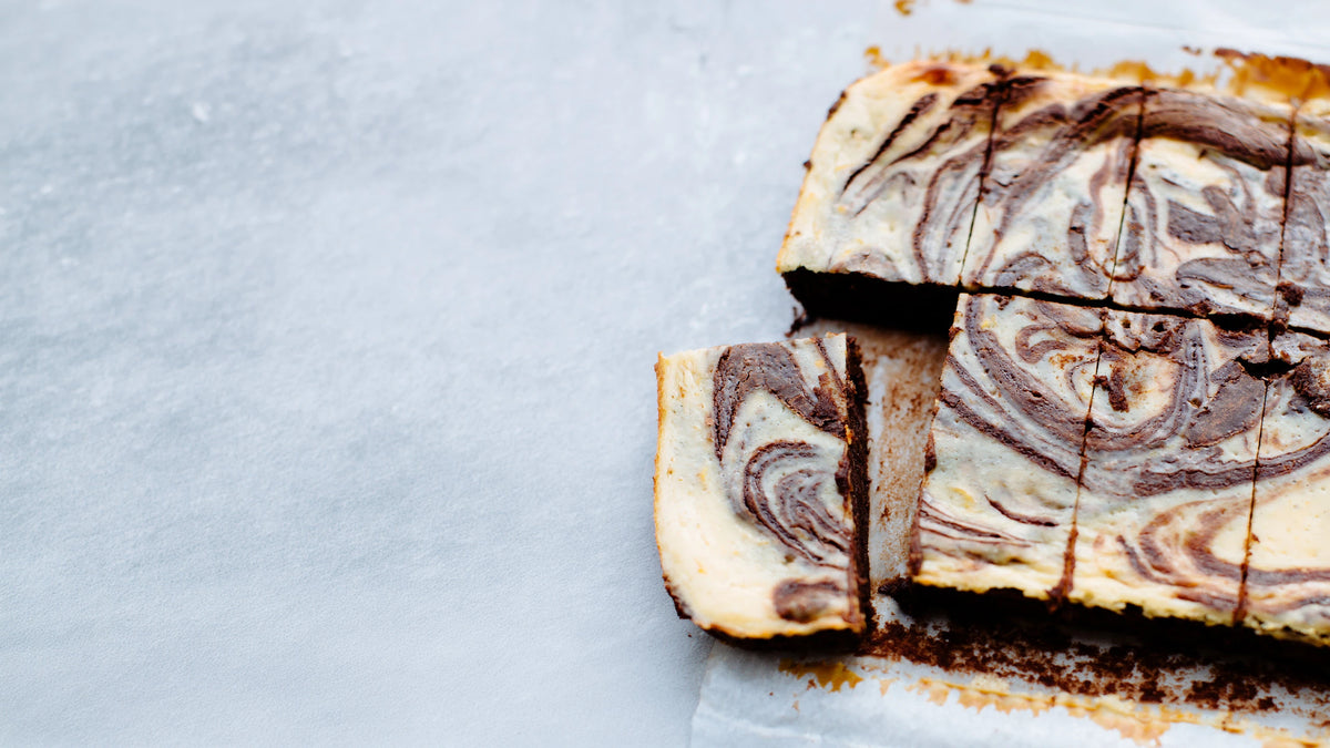 A close-up of a sliced brownie with dark chocolate swirls on a light grey surface, with one slice pulled forward.
